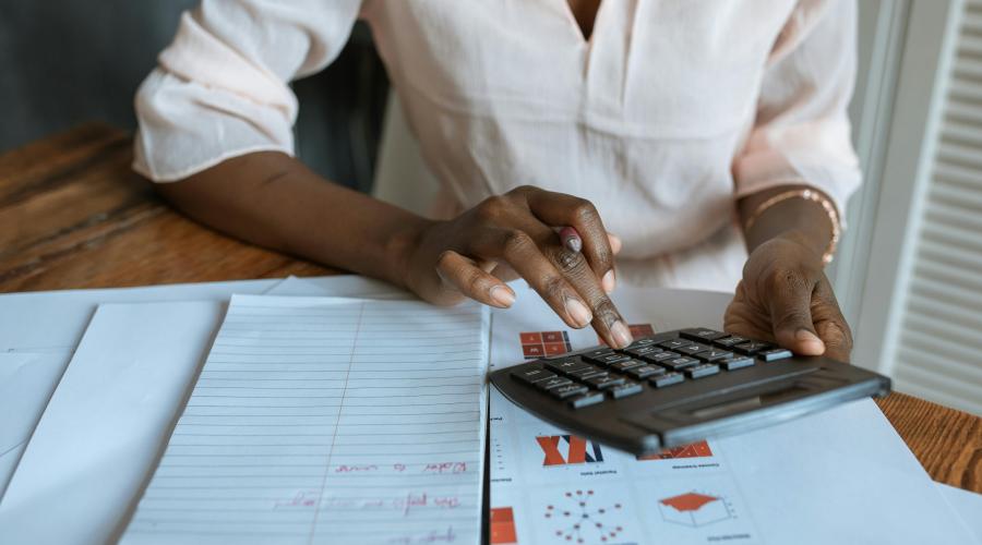 Woman using business calculator with notes and charts sitting on table below her arms