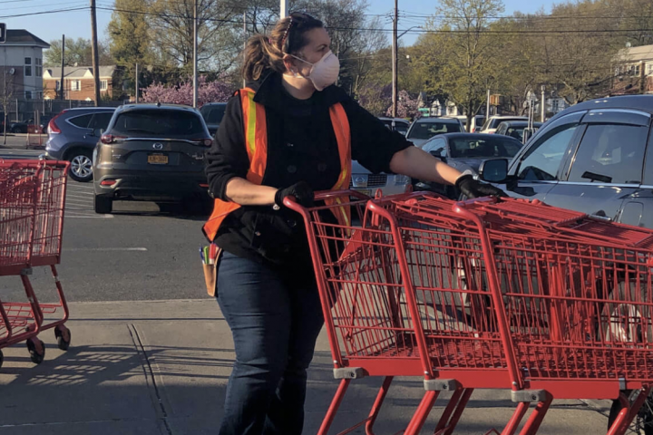Worker with a mask pushes grocery store carts.