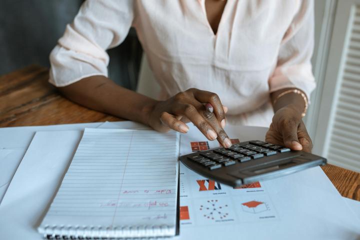 Woman using business calculator with notes and charts sitting on table below her arms