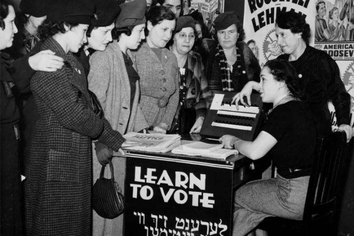 Women are pictured in 1935 teaching other women how to vote, surrounded by posters in English and Yiddish supporting Franklin D. Roosevelt, Herbert H. Lehman and the American Labor Party.