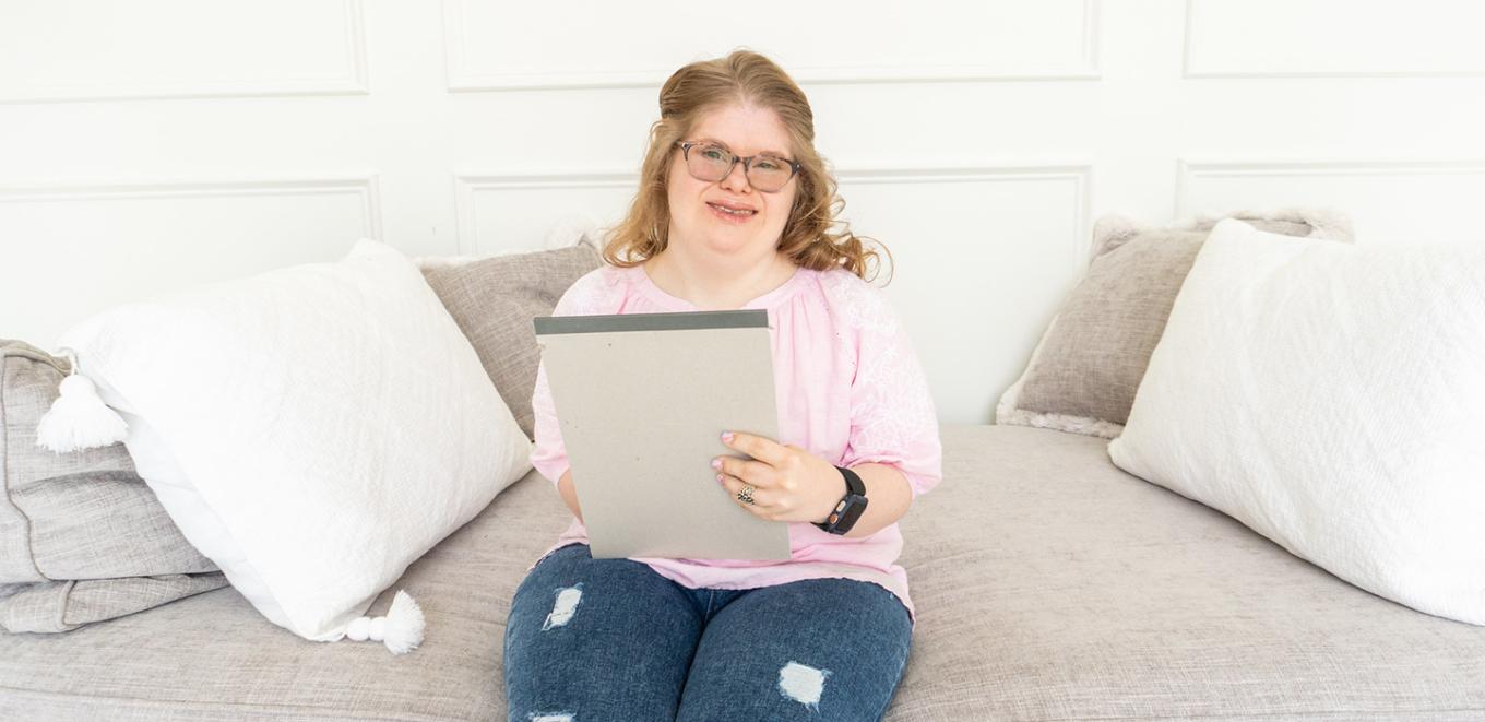 Person wearing pink shirt and glasses using a notepad sitting on a couch in a home setting