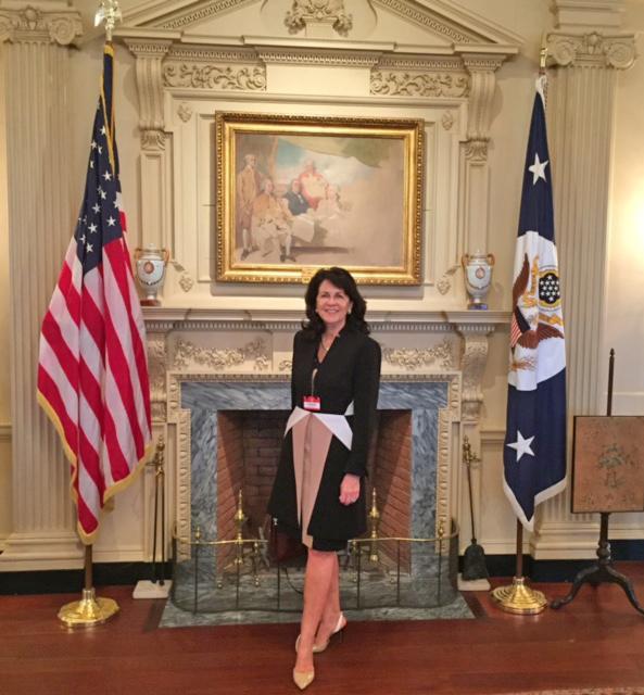 Eva Sage-Gavin standing in front of a fireplace in the White House with flags on either side
