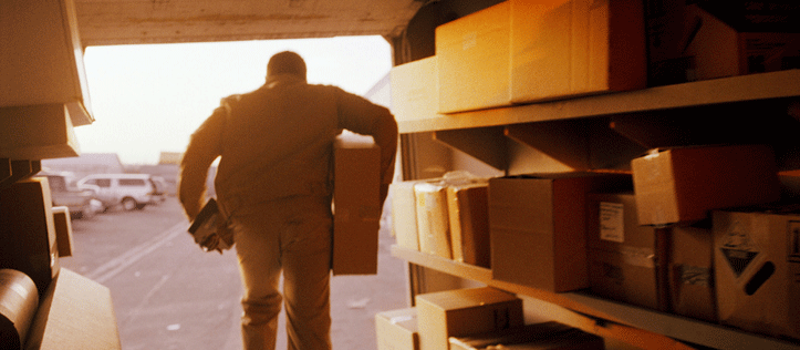 rear view of a delivery man holding a box as he steps out of a box filled van