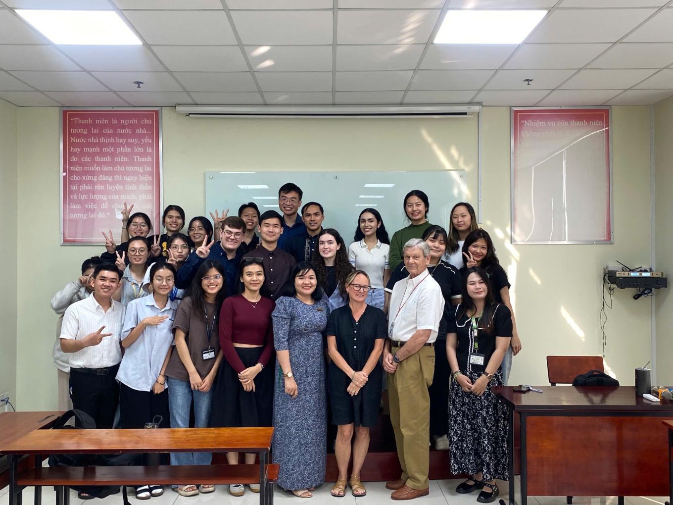 About two dozen smiling students and teachers standing in three rows at the front of a classroom.