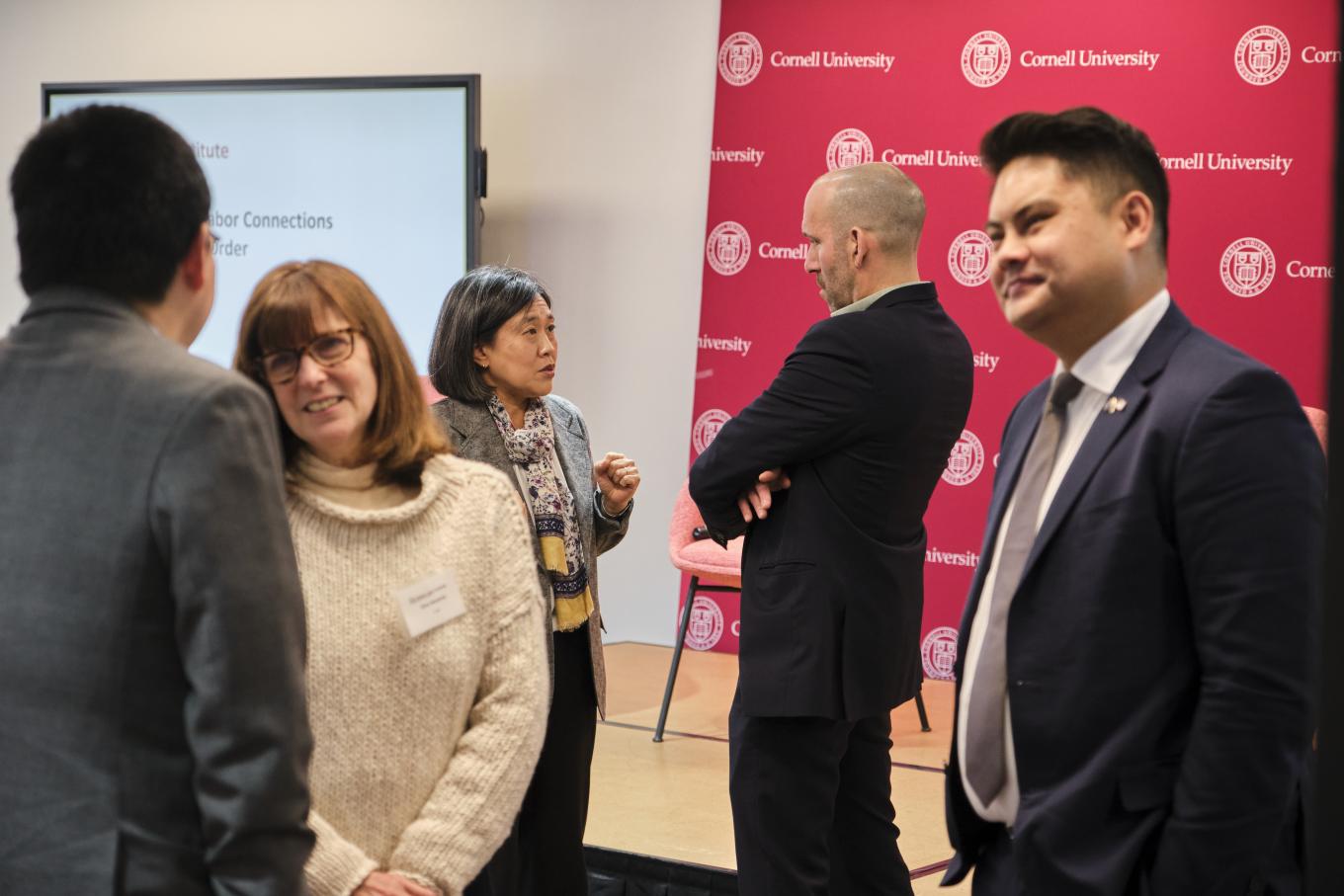 Amb. Katherina Tai and Josh Kagan speak with eachother at the 2025 GLI Conference in New York City, standing at a podium in front of a red backdrop that says 'Cornell University'