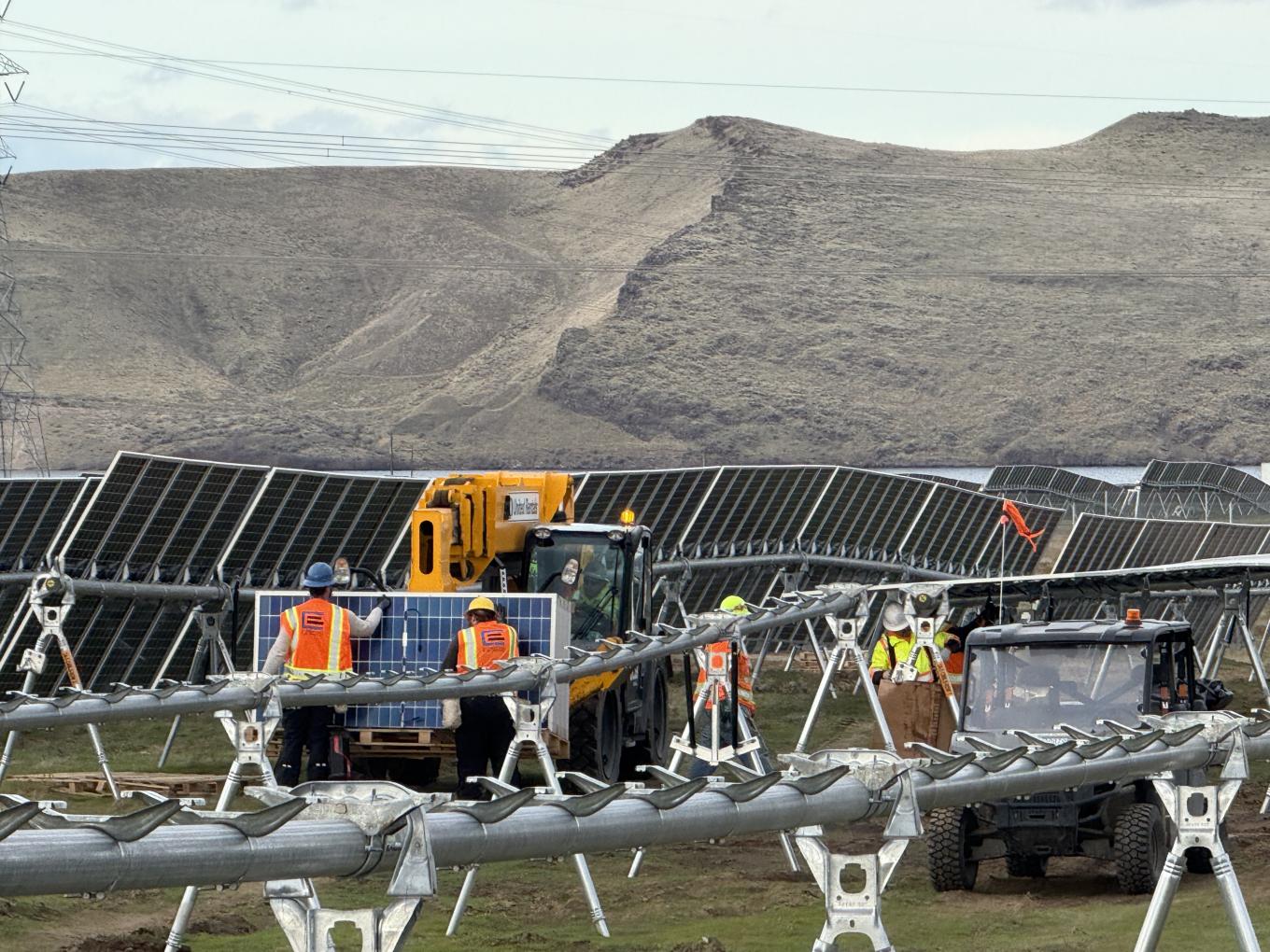 Group of workers in hardhats loading solar panels off crane in a solar farm field