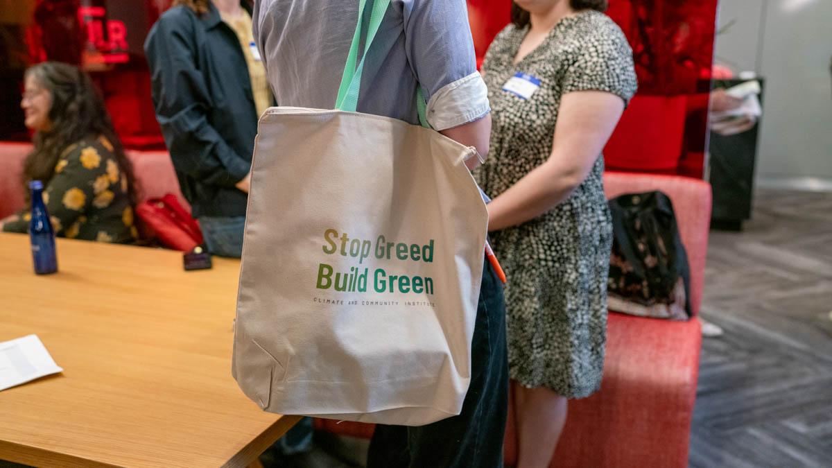 A person wearing a tote bag that reads “Stop Greed Build Green. Climate and Community Institute.”