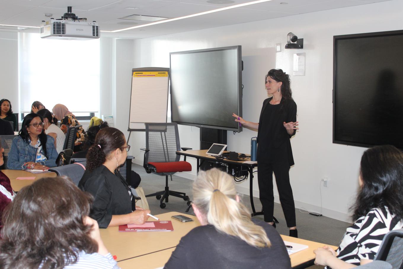 Woman standing in front of classroom speaking to group of women sitting at tables