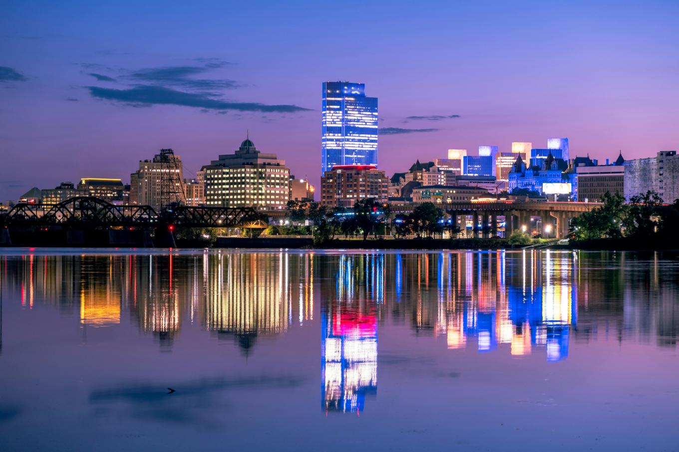 city buildings and lights reflected in a river at dusk