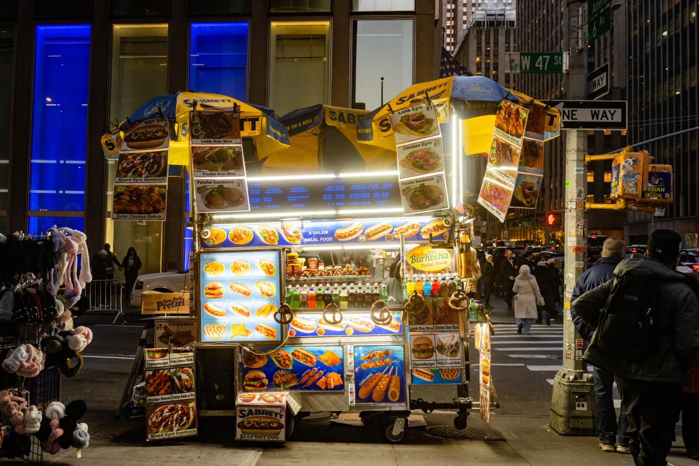 An illuminated hot dog cart is open for business on a Midtown street corner at night.