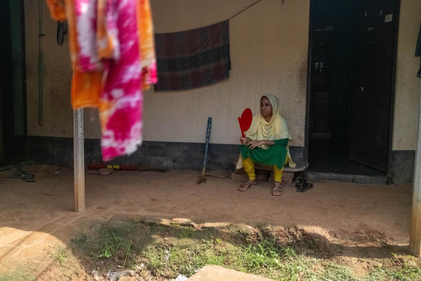 A southasian woman sitting down in front of her house while fanning herself