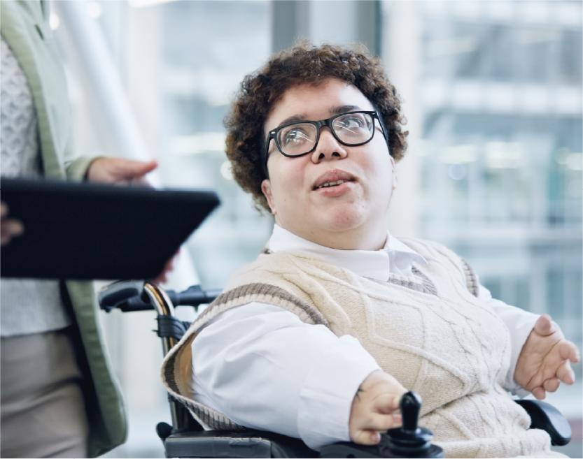 Person in a power chair in an office setting speaking to a person next to them