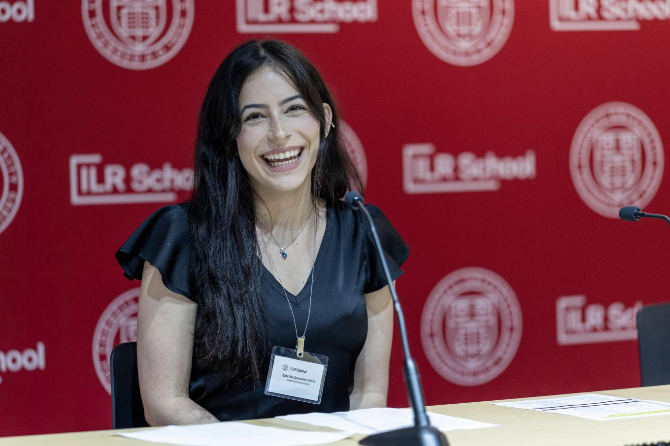 Young woman smiling at camera, sitting behind a desk with mic in front of her