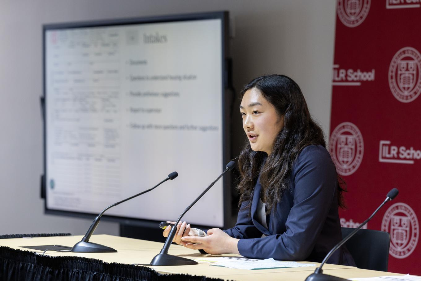 Young woman sitting at desk speaking to off camera group
