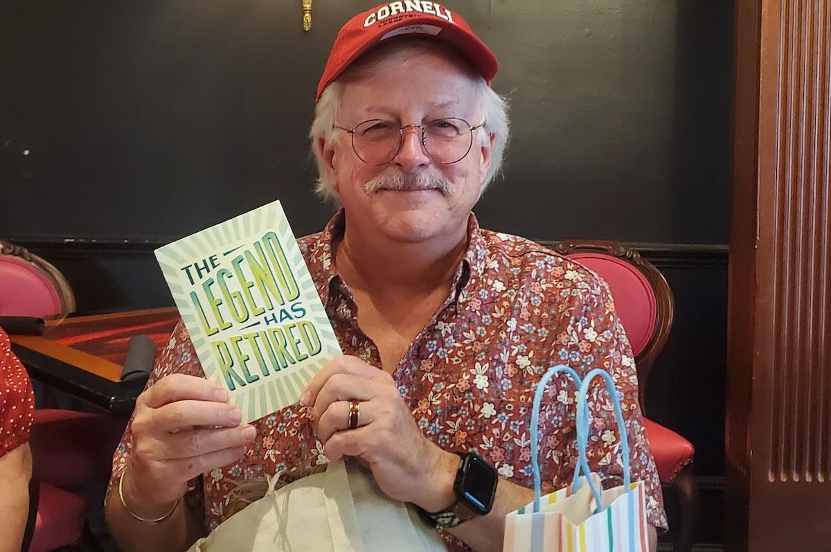 Ray wearing a Cornell baseball cap and holding a retirement greeting card