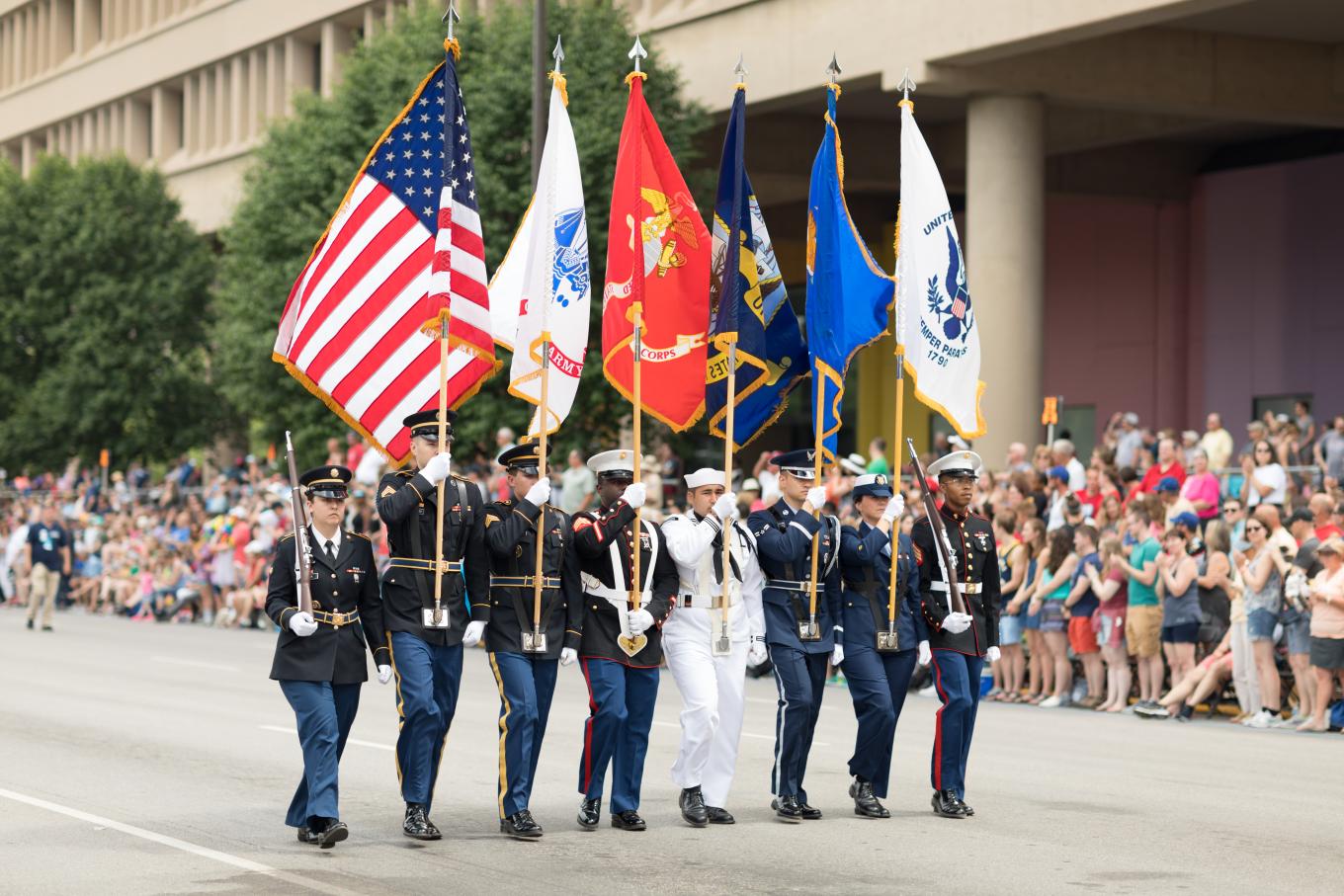 U.S. military personnel wearing uniforms and carrying flags in a parade