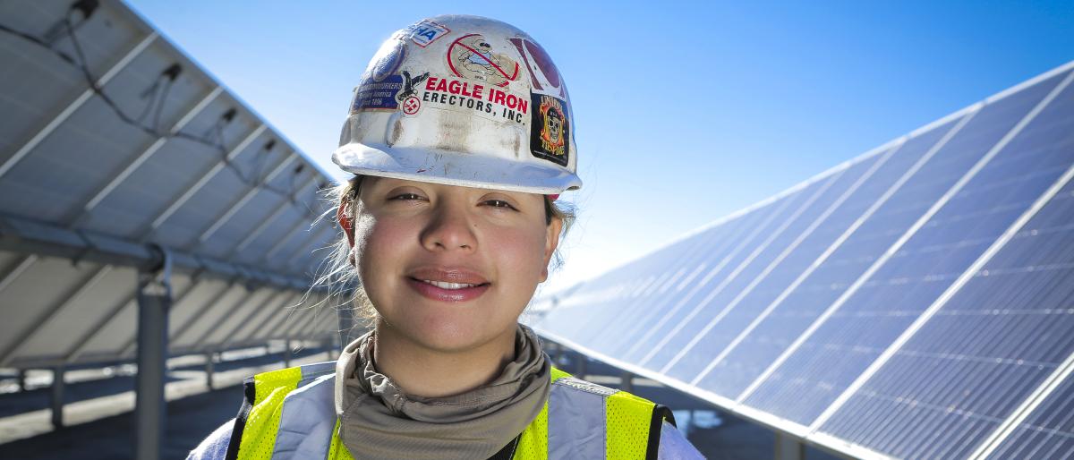 Union woman worker wearing a hard hat and standing in front of solar panels