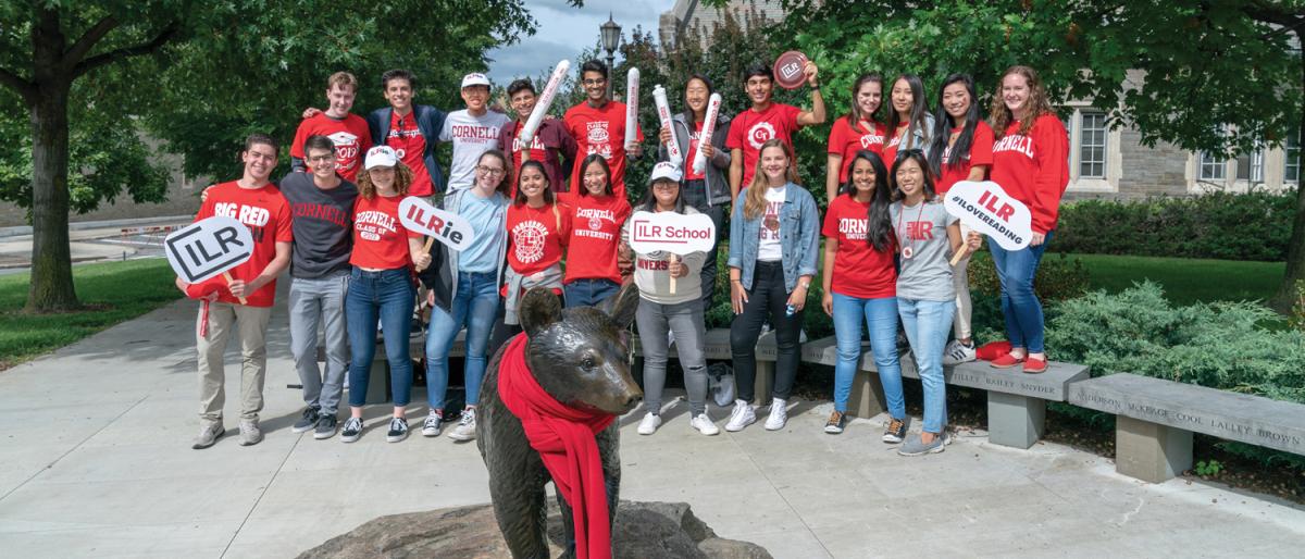 Large group of ILR students posing by Touchdown the Bear statue during Cornell Homecoming.