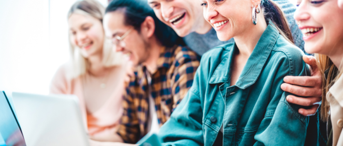 Image of a group of smiling young professionals gathered around a laptop.