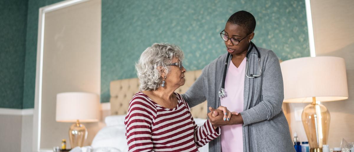 Home care worker standing next to elderly patient assisting them sitting up