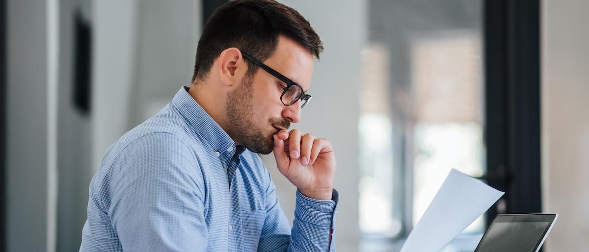 An office worker reviews a sheet of paper while seated at a table.