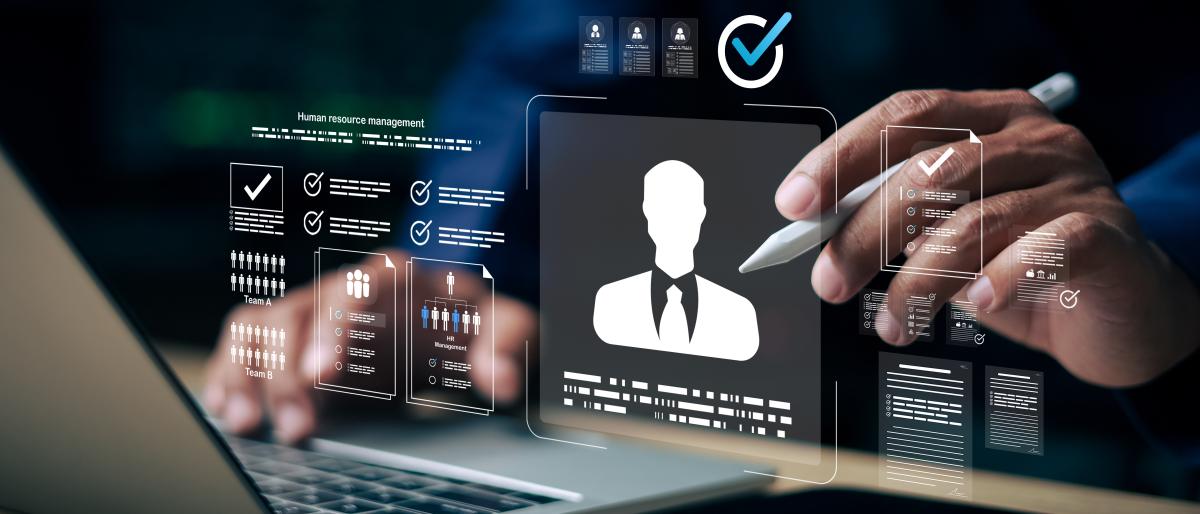A person uses a stylus on a digital tablet beside a laptop, with floating HR technology graphics showing a candidate profile, checkmarks, team icons, and assessment data.