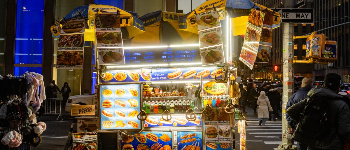 An illuminated hot dog cart is open for business on a Midtown street corner at night.