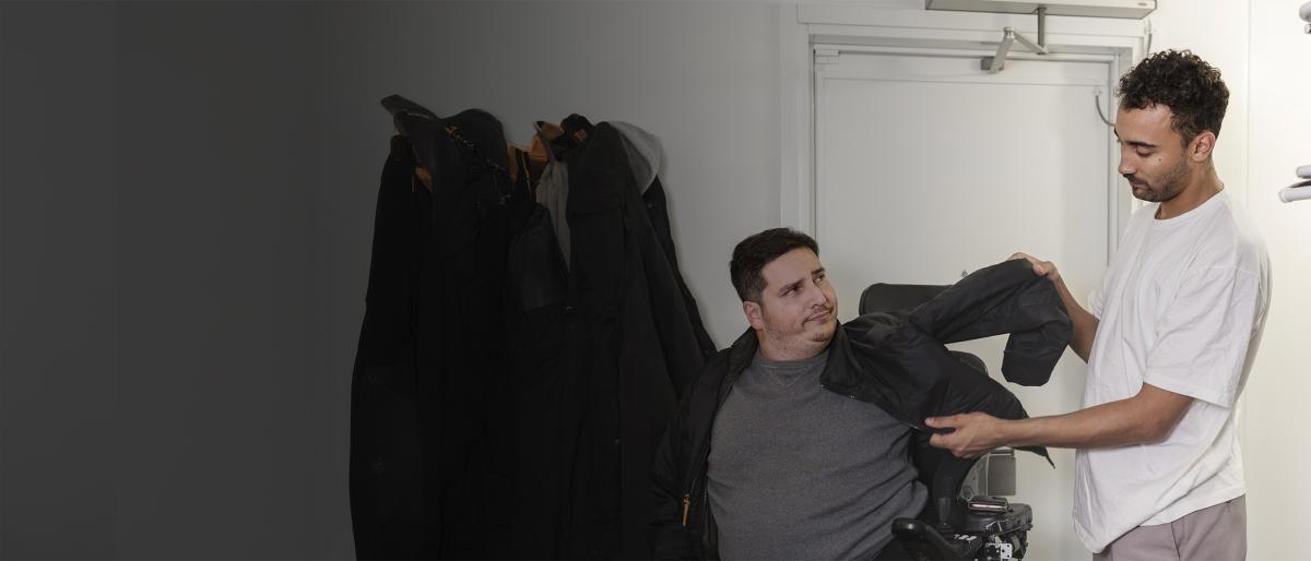 Man assists a man in a wheelchair to put a jacket on before leaving the house the house