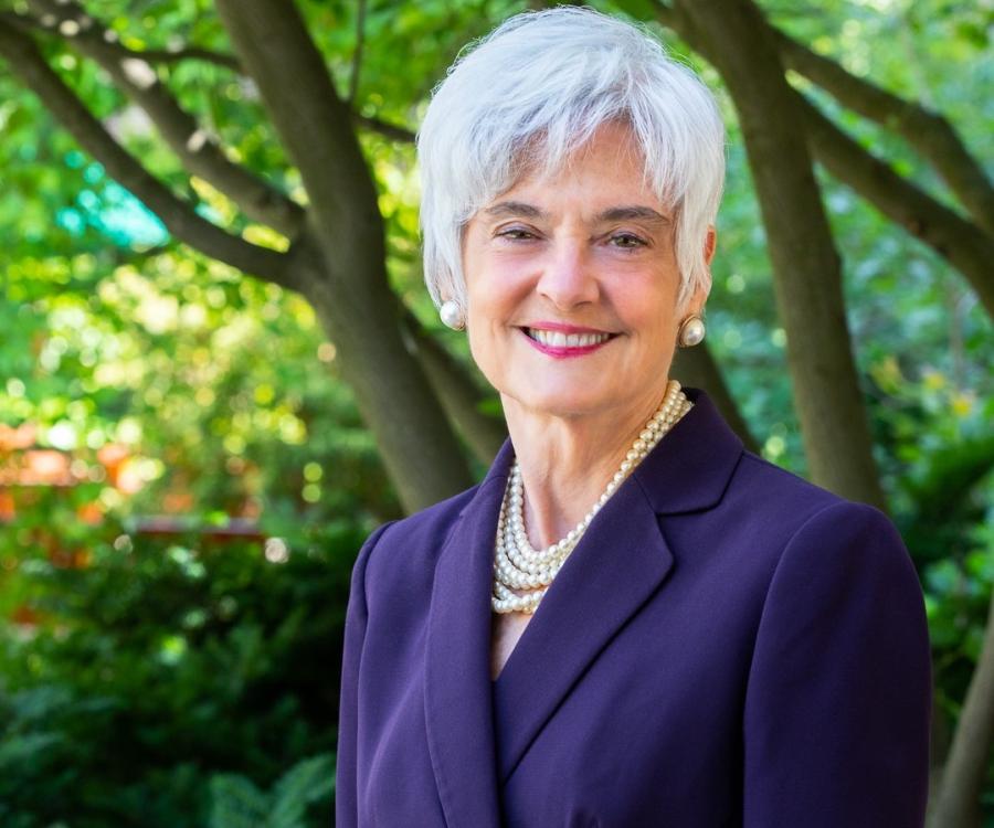 Susanne Bruyère, wearing a purple blazer with several strands of white pearls and matching earrings