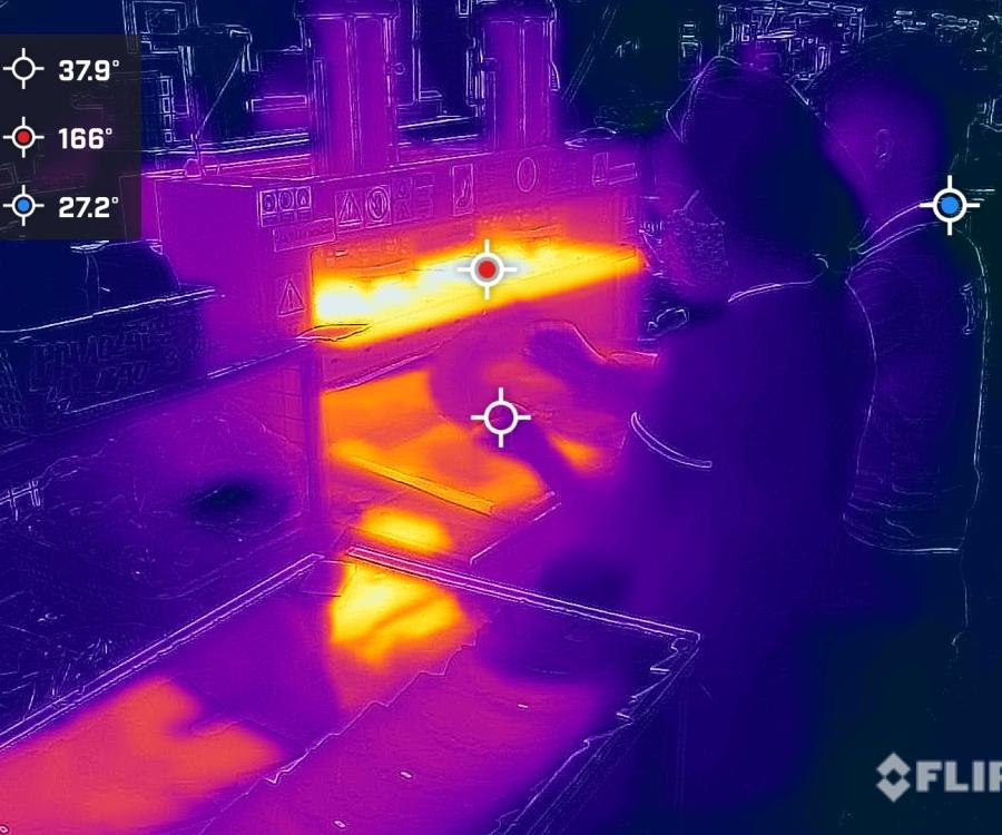 A thermal image of a worker at a station in a garment factory, showing the high heat levels through brighter orange colors at their workstation.