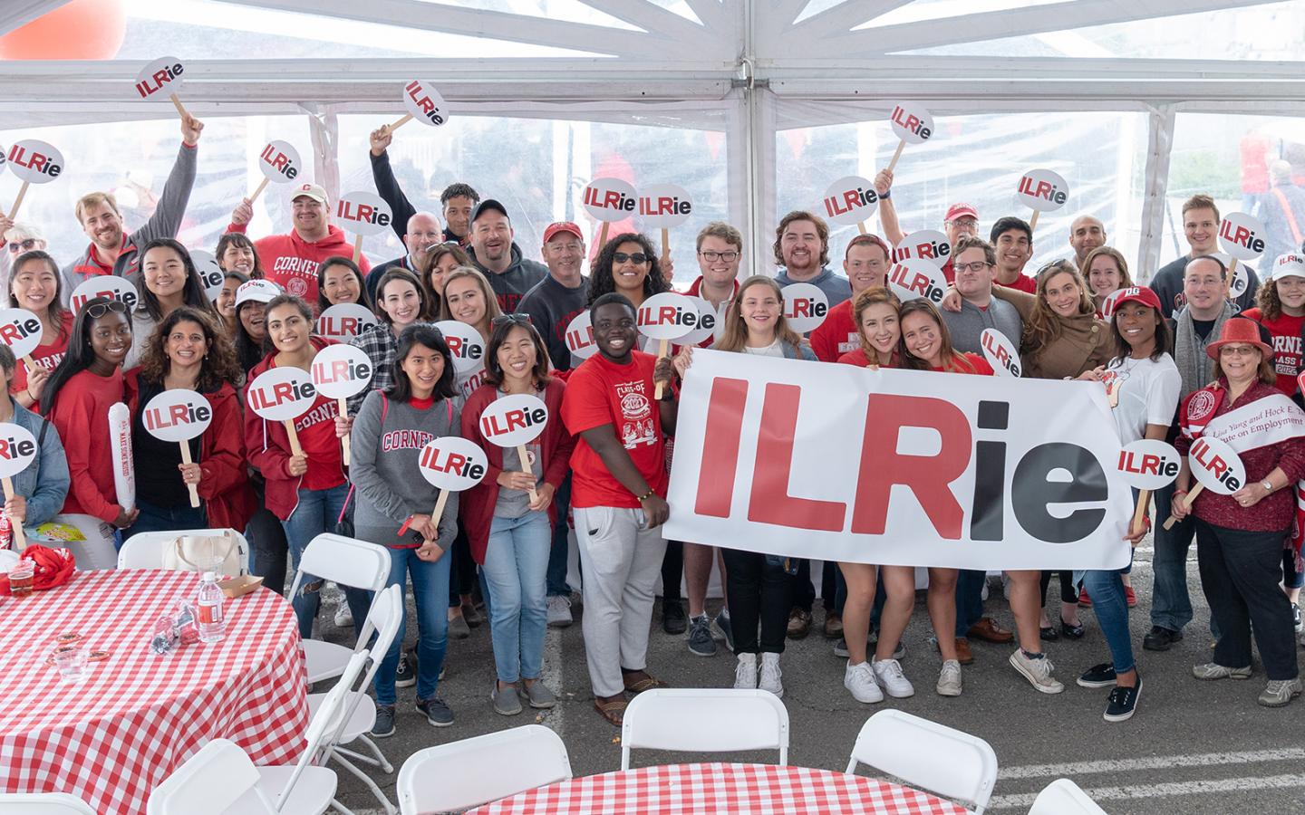 ILR Alumni under a big tent holding up an ILRie banner