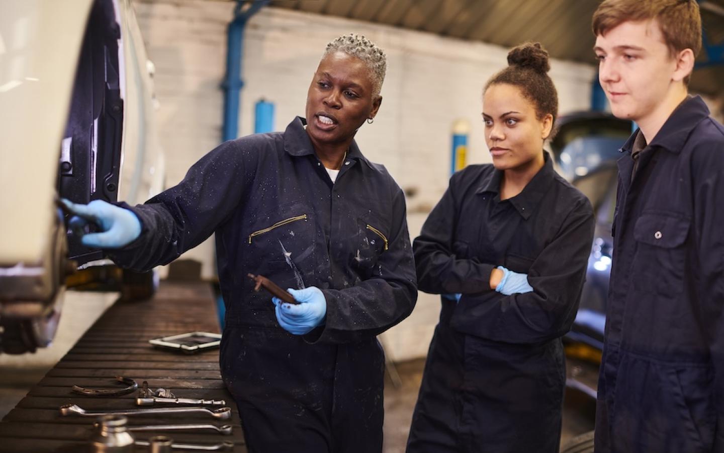 An auto mechanic gives hands-on training to two students