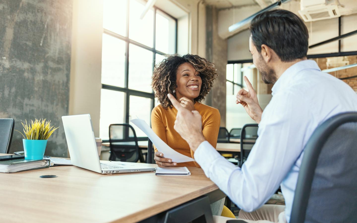 two coworkers having a discussion at a table with a laptop
