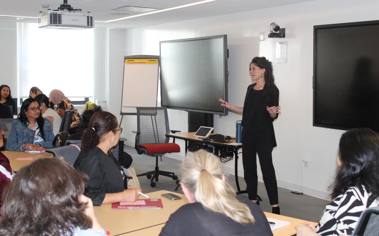 Woman standing in front of classroom speaking to group of women sitting at tables