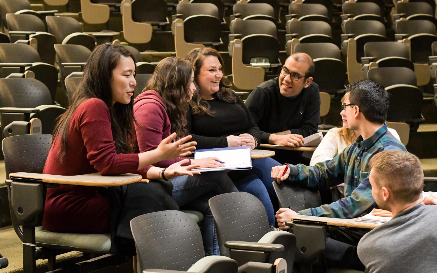 Circle of seven students sit conversing in auditorium seating