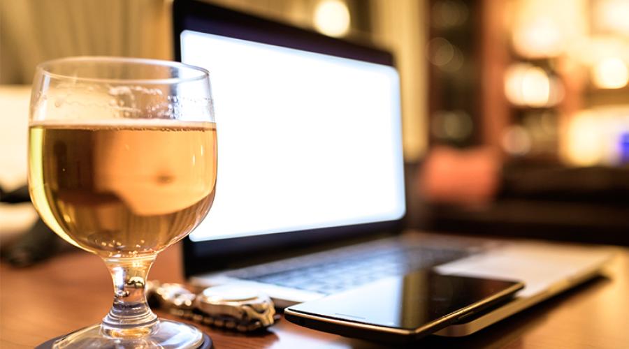 Beer glass next to wristwatch, smart phone and laptop