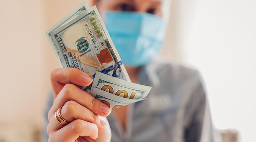 woman wearing surgical mask holding several hundred dollar bills