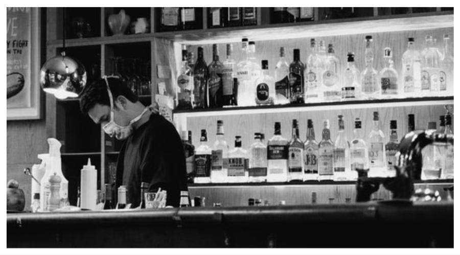 person wearing a mask working behind a bar at a restaurant