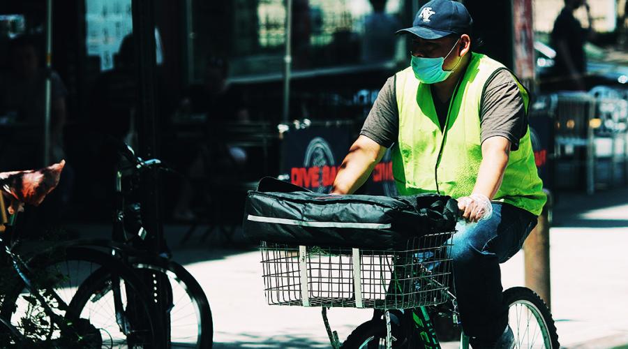 man wearing a mask and high-vis vest riding a delivery bike