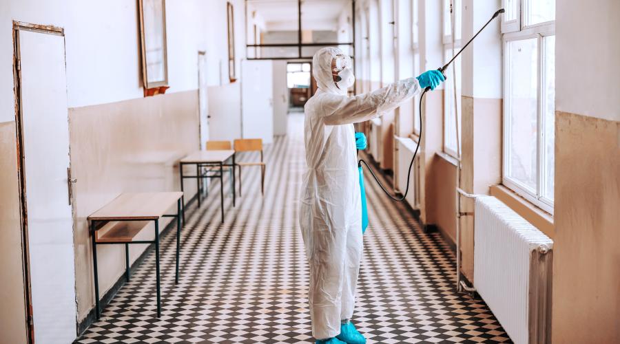 worker-sterile-white-uniform-with-mask-glasses-holding-sprayer-with-disinfectant-spraying-around-hallway-school-prevention-spreading-corona-virus