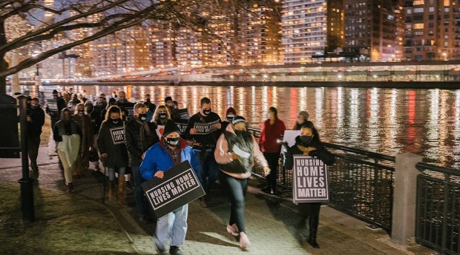 Group of people in NYC holding a night vigil holding signs that say, "Nursing Home Lives Matter".