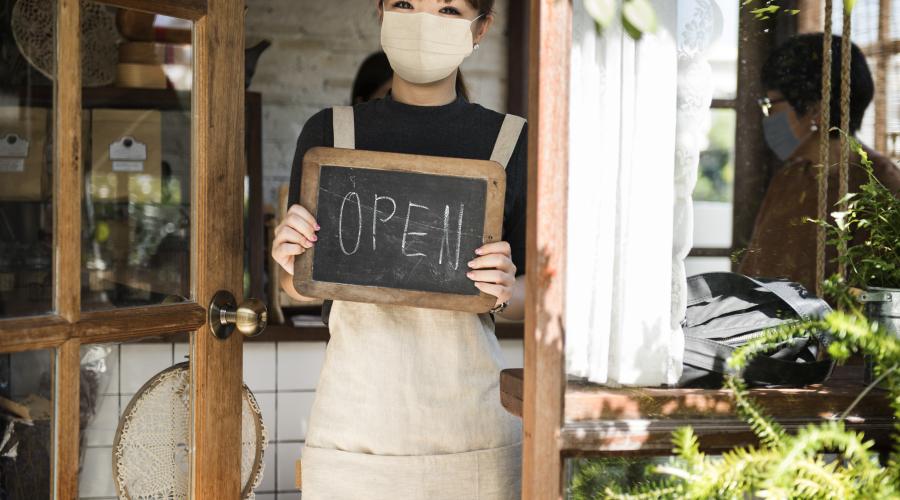 Restaurant worker wearing a face mask holds an "Open" sign