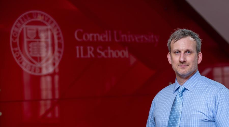 Debate Coach Armands Revelins poses in front of a Cornell Logo