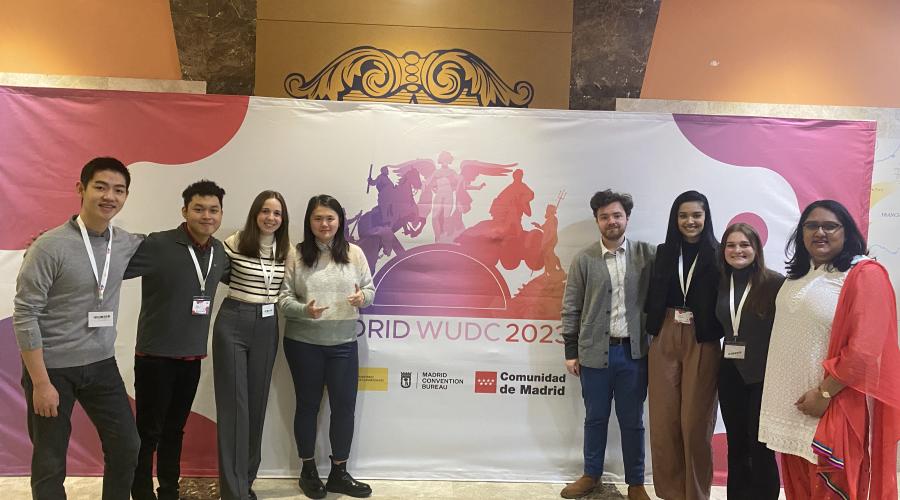 8 Cornellians stand in front of the USUDC Madrid logo