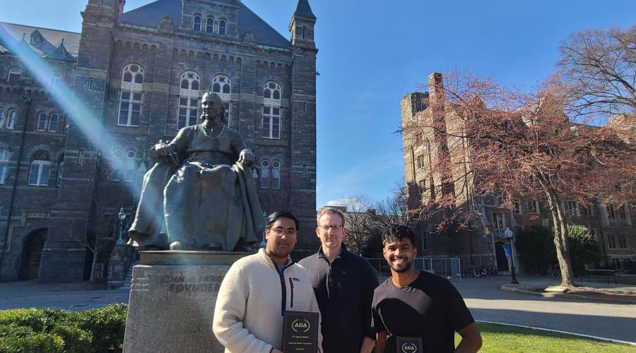 Two Cornell debaters stand with coach in front of a statue at Georgetown 