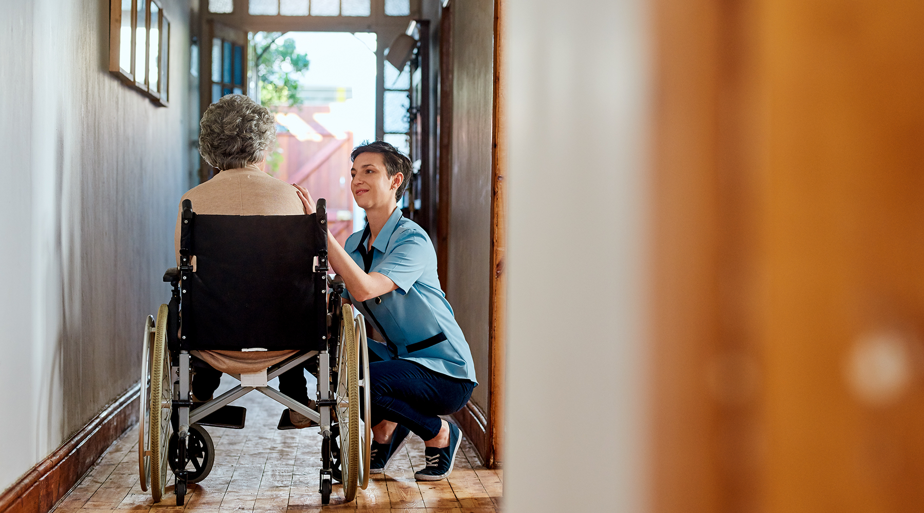 A nurse tends to a wheelchair bound patient in her home