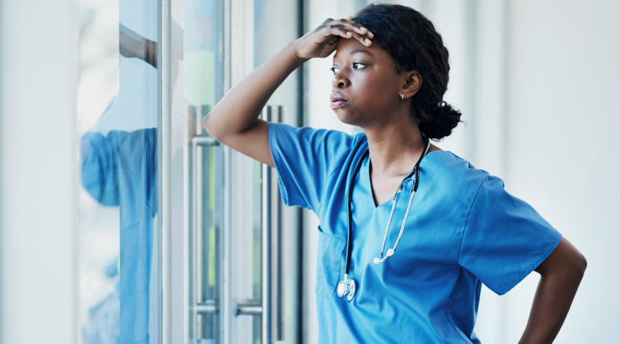 A tired Black nurse looks out a window