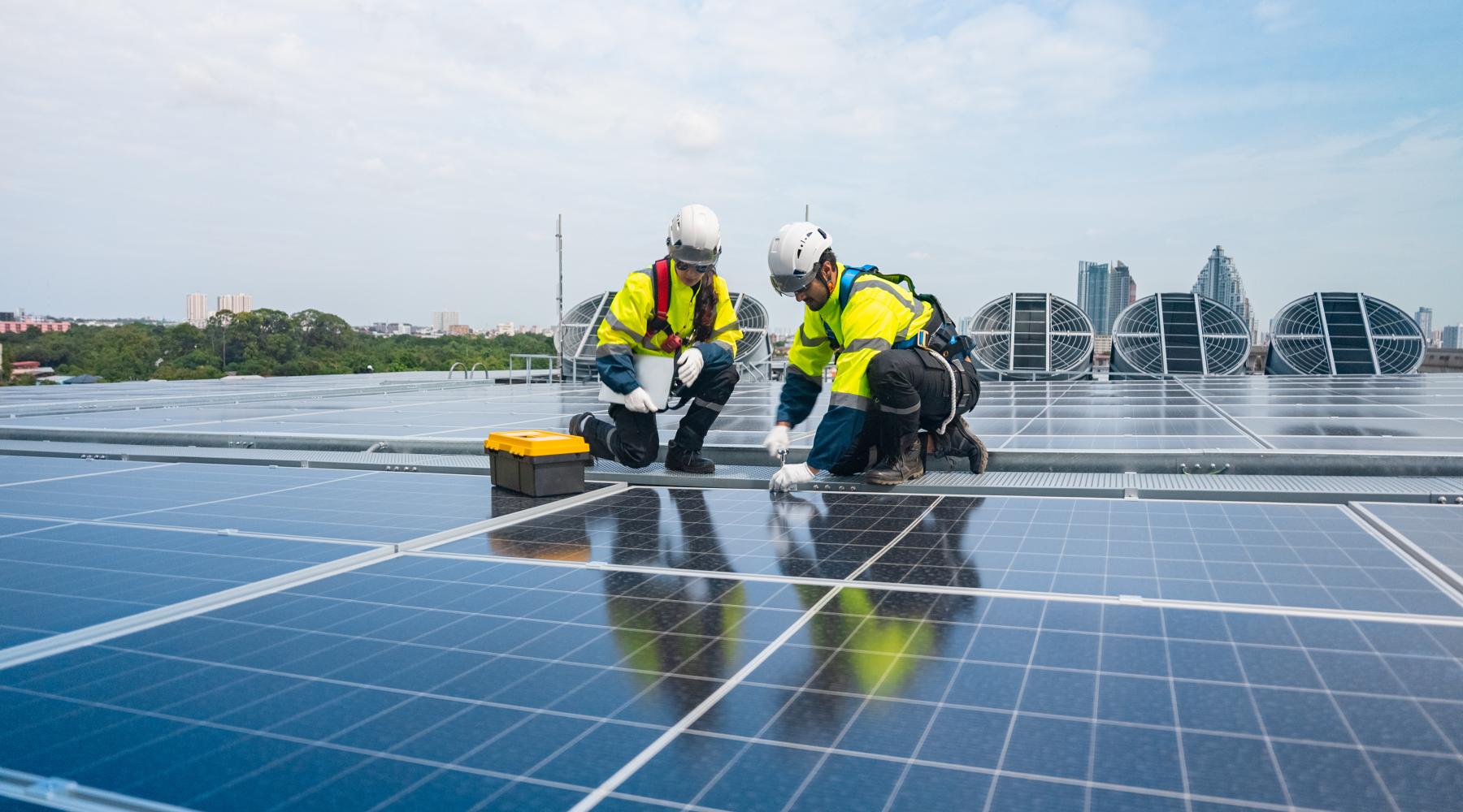 Two technicians wearing hardhats, talking on solar rooftop