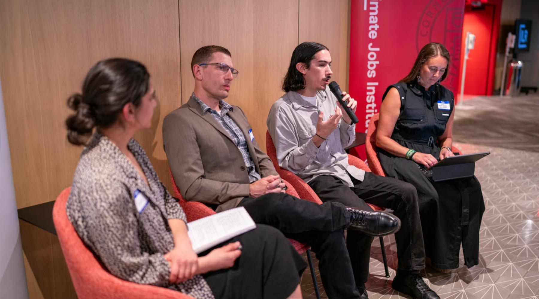 Four panelists seated in a row, with one panelist holding a microphone. A sign in the background reads “Climate Jobs Institute."
