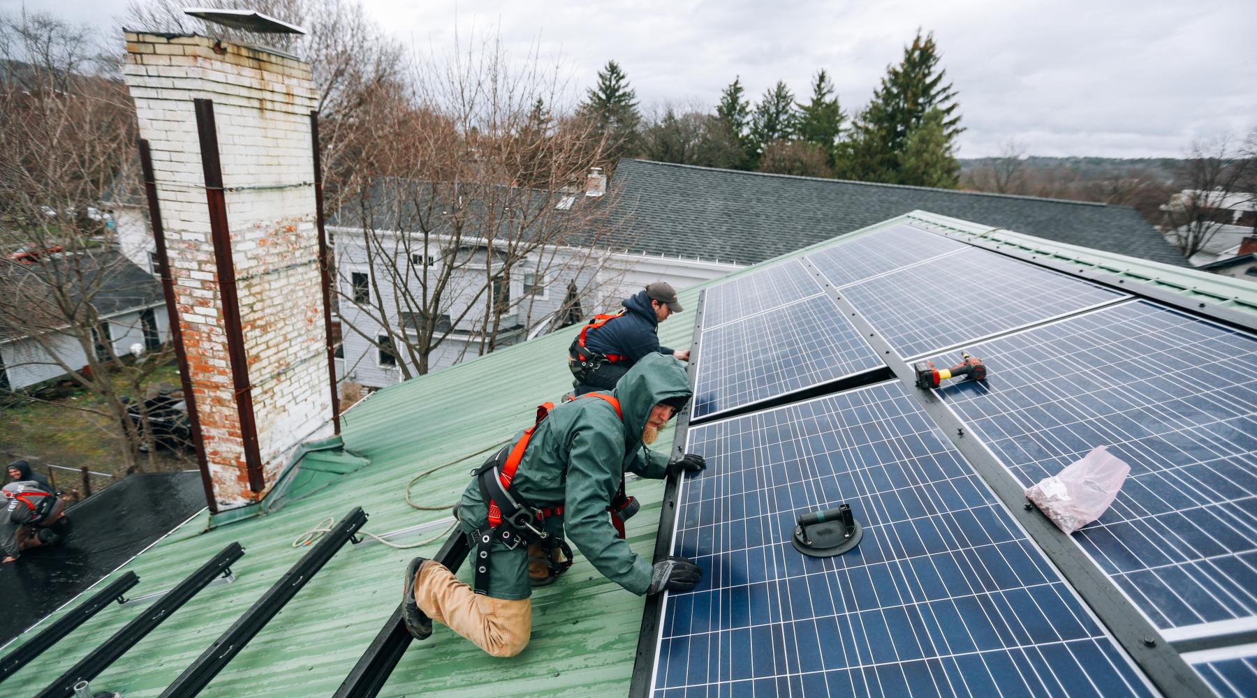 Two men installing solar panels on roof of building